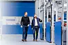 Zwei Männer laufen durch eine Industriehalle mit blauen Maschinenmodulen.