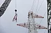 Kran hebt Stahlteil zu Hochspannungsmast mit Arbeitern auf dem Turm