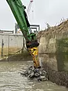 Bagger mit hydraulischem Anbaugerät bricht Beton an einer nassen Schleusenwand